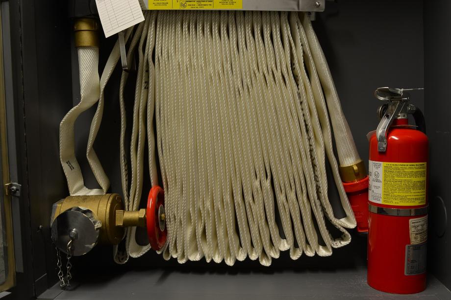 Interior de um abrigo de hidrante: mangueira acondicionada, registro de recalque em latão, carretel e extintor portátil